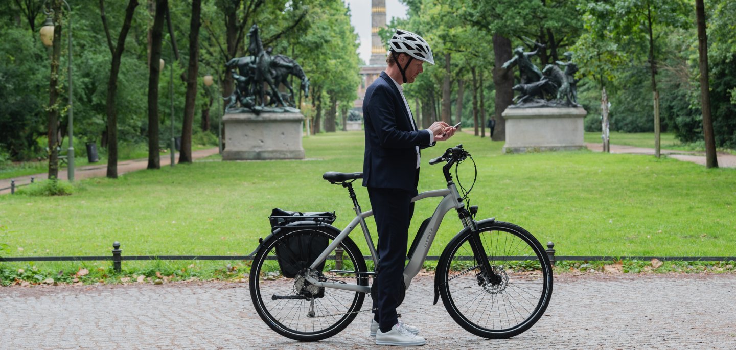 Mann steht mit E-Bike und Handy