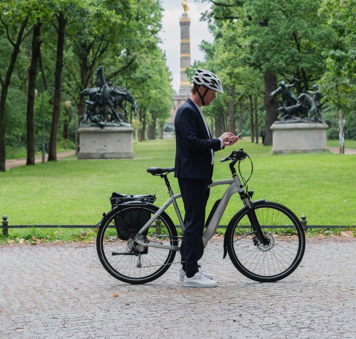 Mann steht mit E-Bike und Handy